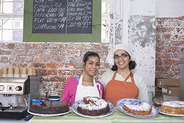 Two women smiling while holding freshly baked bread and pastries - Big Catch Consulting